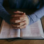 Folded hands in prayer placed on an open Bible