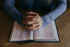 Folded hands in prayer placed on an open Bible