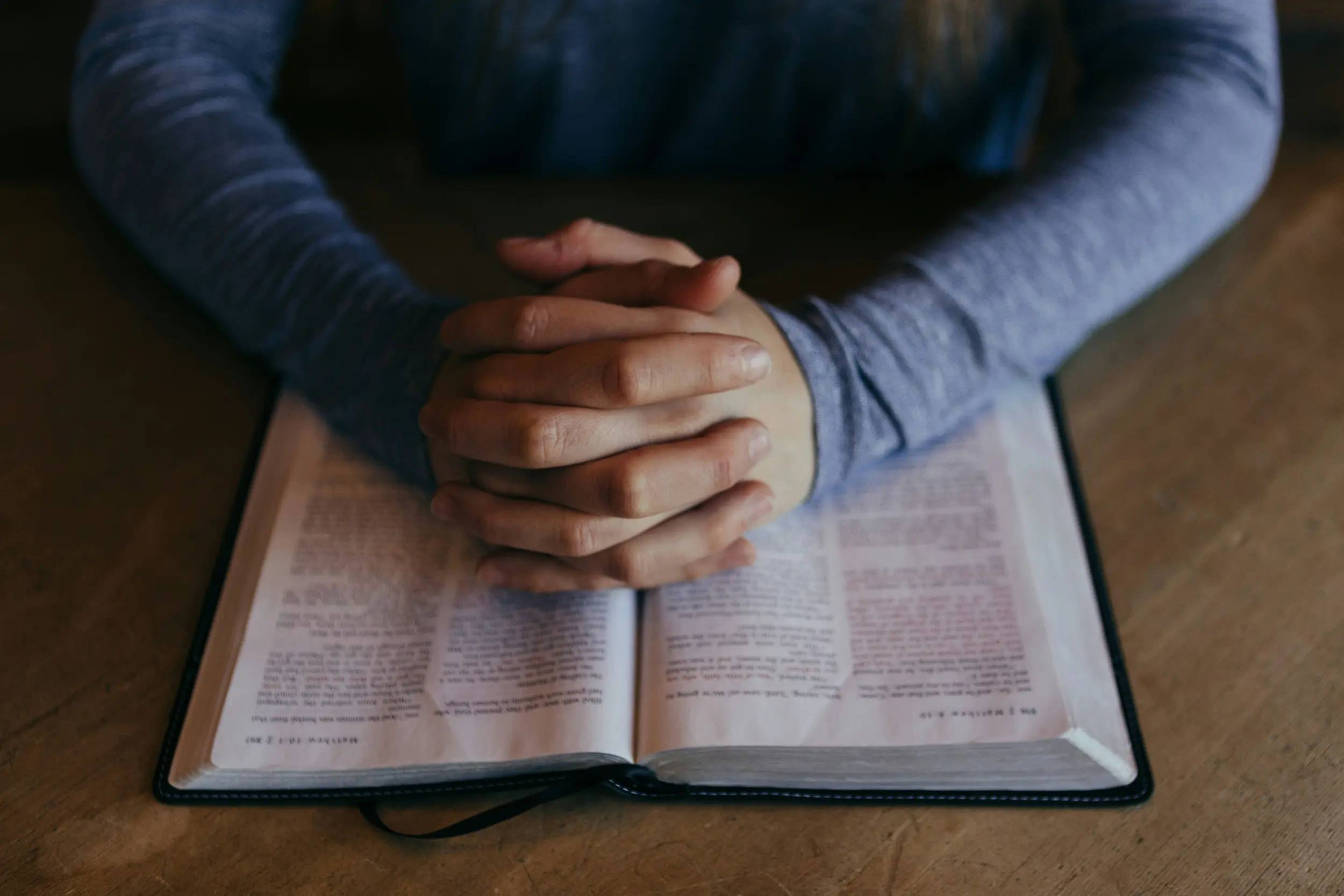 Folded hands in prayer placed on an open Bible